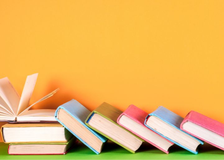 Row of colorful books leaning against each other with one open book on a bright background